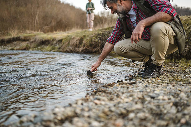 istock man hiker backpacker kneel by a creek and filling a mug with water 2205139749