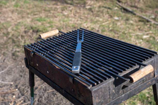 istock Set of BBQ tools. Barbecue tools (tongs, carving fork, spatula). Close-up of an open empty barbecue grill with a large fork, spatula and tongs on top outdoors. 2205141327
