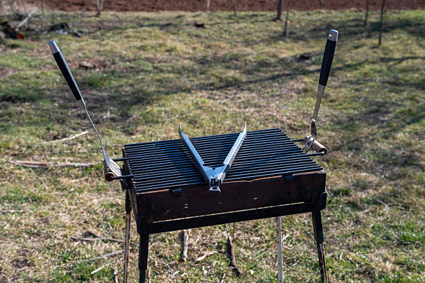 Set of BBQ tools. Barbecue tools (tongs, carving fork, spatula). Close-up of an open empty barbecue grill with a large fork, spatula and tongs on top outdoors.