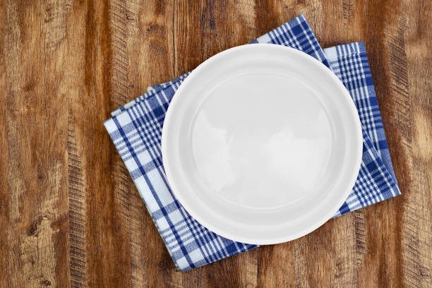 istock White ceramic plate on a rustic wooden table with blue checkered napkin. 2205143380