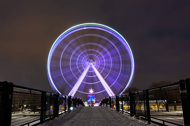 A captivating nighttime shot of the Ferris wheel at the Old Port of Montreal, illuminated with colorful lights, creating a vibrant and magical atmosphere against the dark sky.