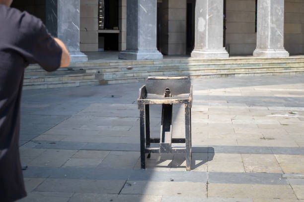 A person tosses a coin toward an old iron toad game in a village square, sapo game