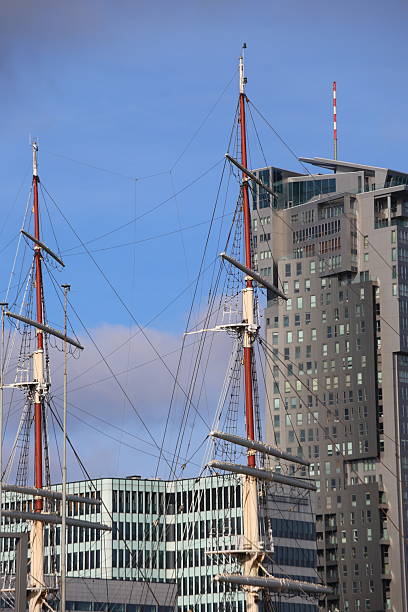two masts of a sailing ship with a skyscraper and sky in the background