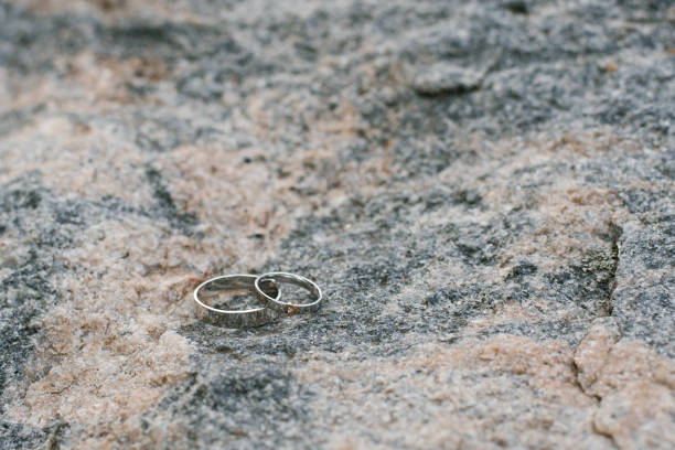 A pair of silver wedding rings placed on a textured stone surface outdoors, symbolizing love and commitment.