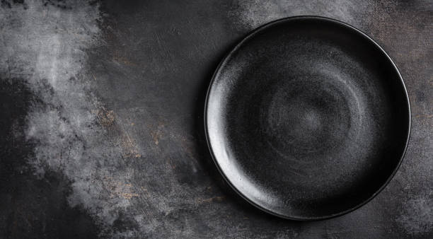 Black plate on textured black background. Long banner format. top view. Copy space