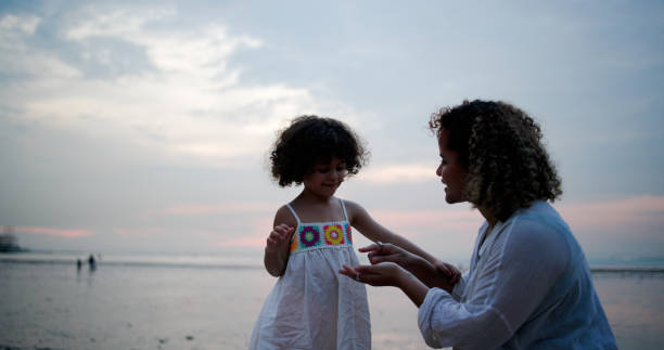 Happy Mother And Daughter in casual suits playing with shellfish  While Enjoying the Weekend With Family at the Beach
