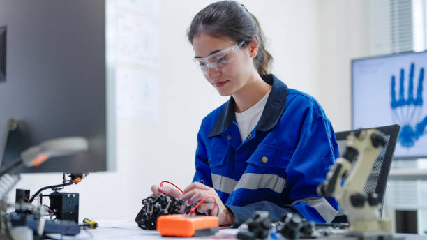 istock White woman engineer developer wearing safety protective goggles with blue work jacket is soldering intricate robotic components on a circuit board or an electronic device workshop in a laboratory room 2205172459