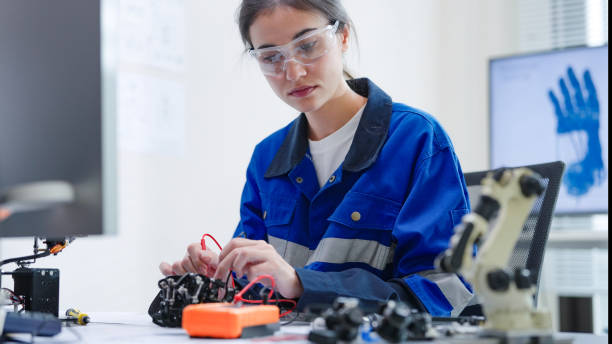 istock White woman engineer developer wearing safety protective goggles with blue work jacket is soldering intricate robotic components on a circuit board or an electronic device workshop in a laboratory room 2205172462