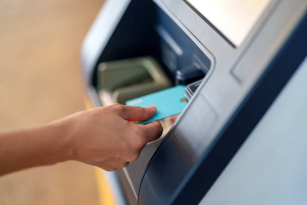 A close-up shot of a person inserting a blue debit or credit card into an ATM machine for a financial transaction.
