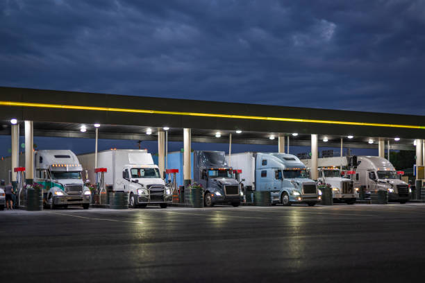 Different big rig semi trucks with turned on headlights and loaded semi trailer standing on the truck stop gas station at night time fill up the trucks tanks to continue their routes in the morning stock photo
