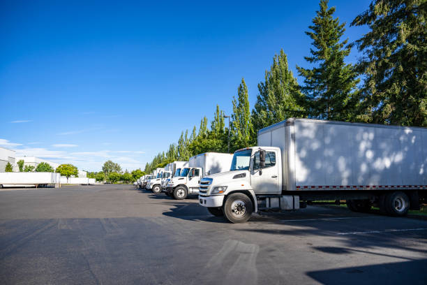 istock Industrial grade middle duty day cab rigs semi trucks with box trailers standing in row on warehouse parking lot waiting for the next local deliveries 2205185135