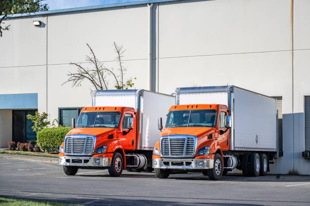 istock Orange day cab middle duty rigs semi trucks with box trailers standing in warehouse dock gates loading cargo for the next local delivery 2205185189