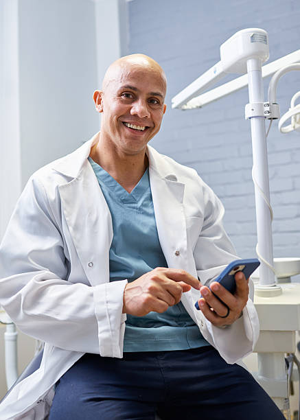 istock Friendly Smiling Male Dentist in a Clinic Setting Using a Smartphone 2205186818