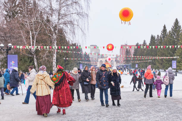 Yekaterinburg, Russia - March 2, 2025: People enjoying Maslenitsa celebration in city park. Park decorated with colorful banners and sun-shaped ornaments. Farewell to winter, arrival of spring.