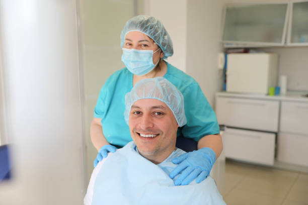 The beautiful smile of a satisfied young man in the dental office, next to him is a middle-aged female dentist.