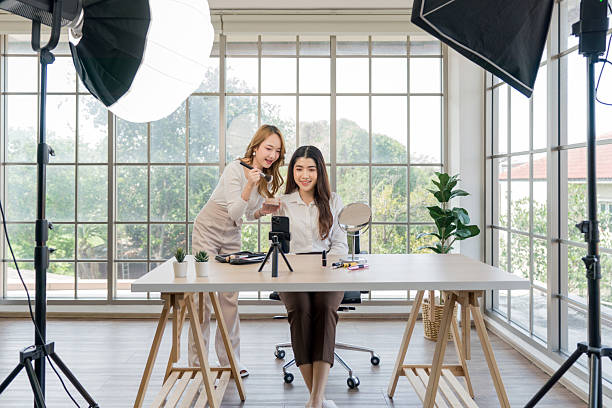 istock Two asian women creating content for social media. They are using a studio setup that include a smartphone mounted on a tripod, lighting equipment and various makeup product arrayed on the table. 2205198738