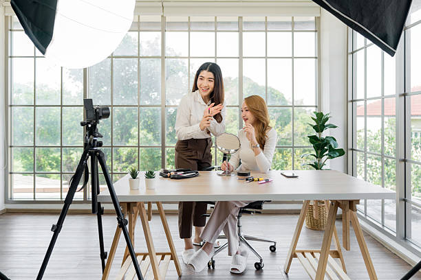 istock Two asian women creating content for social media. They are using a studio setup that include a camera mounted on a tripod, lighting equipment and various makeup product on the table. 2205198740