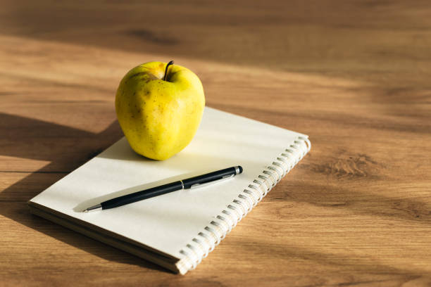 Apple, notebook and pen on wooden table close-up. Back to school concept. Healthy breakfast and snack at work.