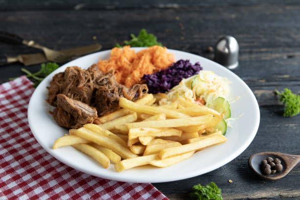 Stock photo showing close-up view of a meal of chicken cheeseburger in a white, sesame seed bread burger bun on a white plate served with crunchy French fry chips and a ramekin of tomato ketchup.