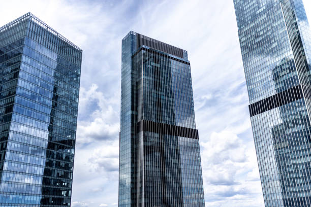 Contemporary tall buildings with reflective glass exteriors under a partially cloudy blue sky, showcasing an urban architectural design.