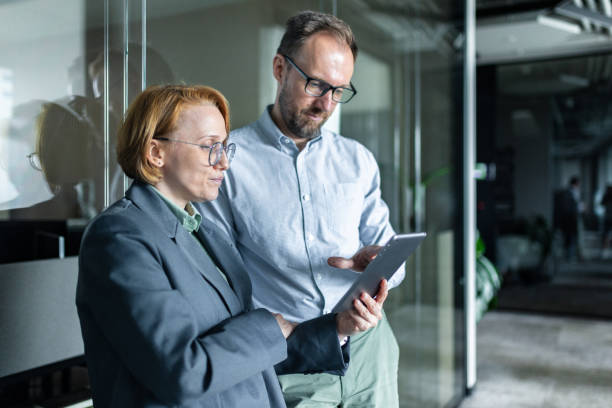 istock Two Business Professionals Discussing Information on a Tablet in a Modern Office 2205209819