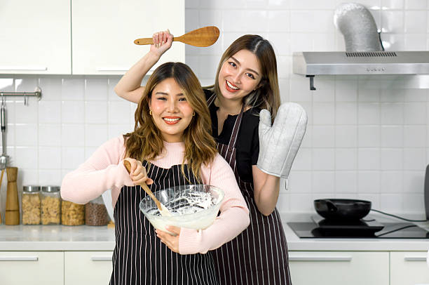 istock Two women are having fun baking together. They are wearing apron and smiling while mixing ingredients with a wooden spoon. 2205215345