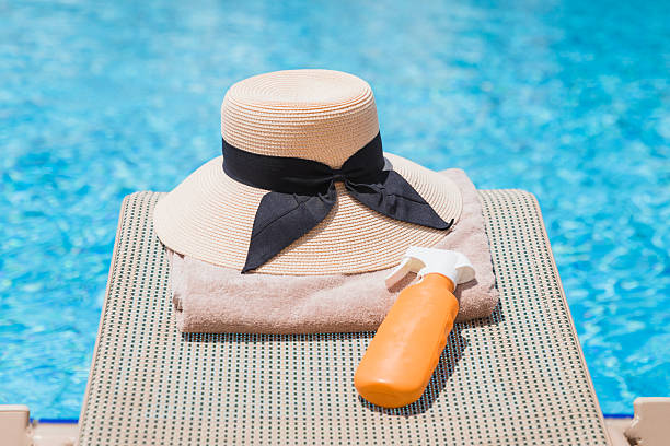 istock Hat, towel and suntan lotion on a swimming pool deck chair 2205217717