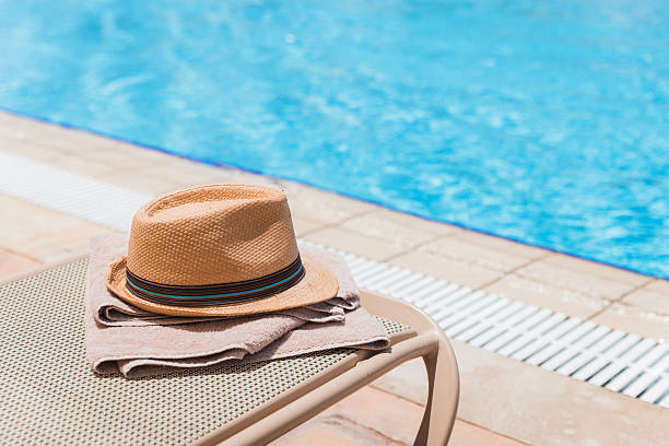 istock Sun hat and towel on a swimming pool deck chair 2205217764