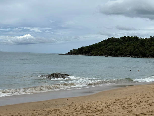 istock Tranquil Beach Landscape With Gentle Waves and Distant Hills Under a Cloudy Sky 2205219242