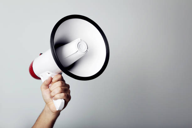 istock Female hand holding megaphone on grey background 2205220386