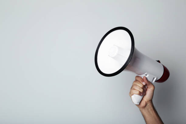 istock Female hand holding megaphone on grey background 2205220504