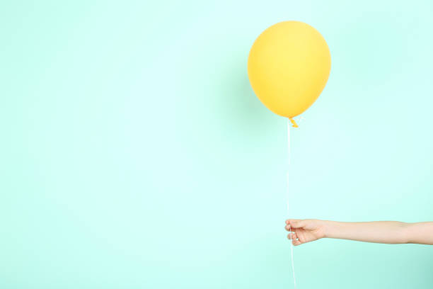 istock Female hand holding yellow balloon on mint background 2205221219