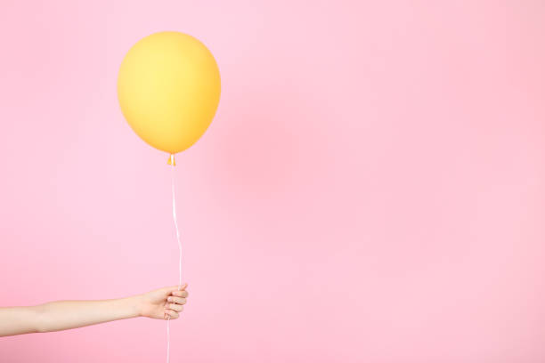 istock Female hand holding yellow balloon on pink background 2205221285