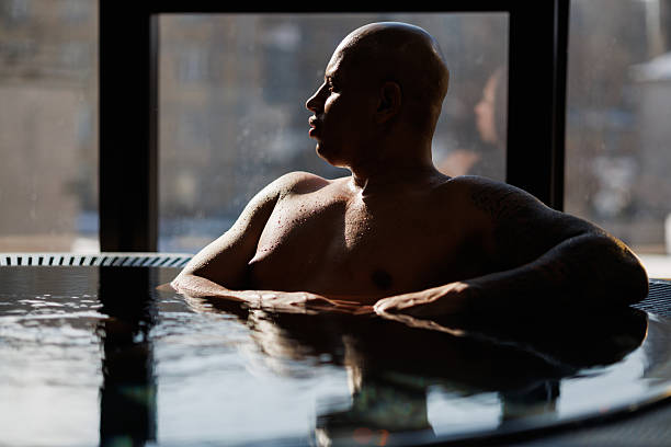 istock Muscular african american man relaxing in hot tub near window in spa 2205225764
