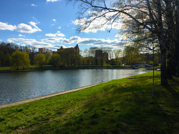 A tranquil park scene with a serene river mirroring trees and urban structures.