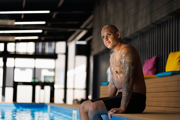 istock Tattooed african american man sitting at poolside in spa complex 2205226396