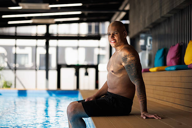 istock Tattooed african american man smiling at camera at poolside in spa complex 2205226400