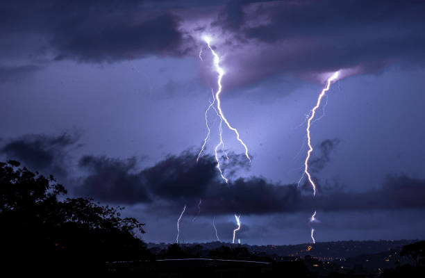 a dramatic lightning bolt illuminates the night sky above a suburban neighborhood, casting a purple glow over the horizon - kuvvetli yağmur stok fotoğraflar ve resimler
