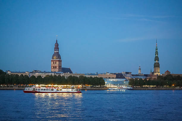 Riga Old Town on cool blue evening sky background with a boat with bright lights swimming in the Daugava river, Riga, Latvia