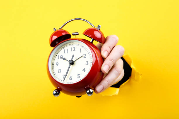 istock Hand holding alarm clock from yellow torn paper 2205247793