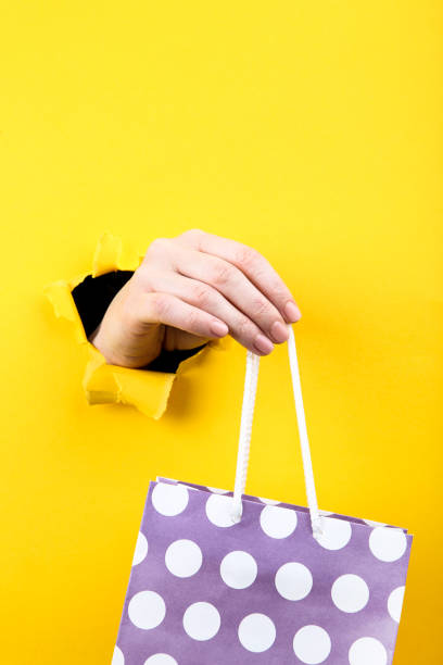 Hand holding shopping bag from yellow torn paper