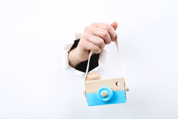Hand holding wooden camera toy from white torn paper