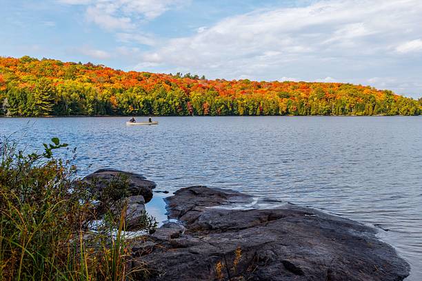 Two people in a distant canoe on a calm lake surrounded by fall colors in Algonquin Provincial Park