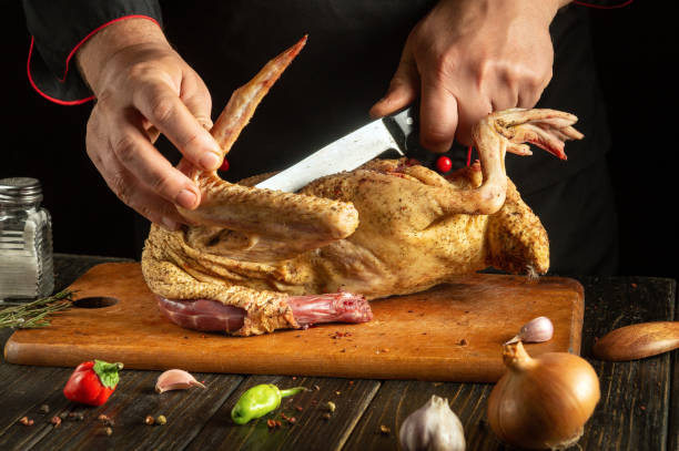 istock A skilled chef uses a sharp knife to cut raw poultry on a wooden cutting board. Fresh herbs, garlic, and chilies surround the area, showcasing a vibrant culinary setting 2205251896