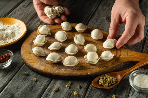 istock Hands skillfully shape dumplings on a wooden board, surrounded by ingredients like flour and spices. The process showcases traditional cooking techniques 2205252002
