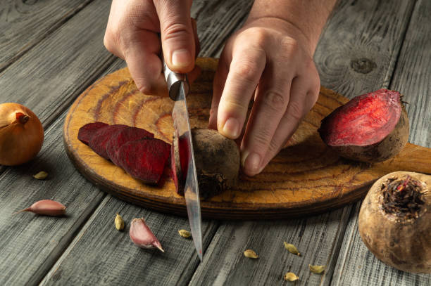 istock Hands skillfully slice vibrant beets on a rustic wooden cutting board. Nearby, garlic cloves and halved onions complement the fresh produce, enhancing the cooking process 2205252130