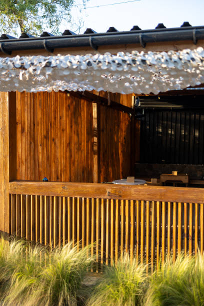 istock A rustic wooden bar with slatted panels is bathed in warm sunlight. A white decorative net hangs above, casting soft shadows. Tall grasses in the foreground add natural touch to cozy outdoor setting 2205253401