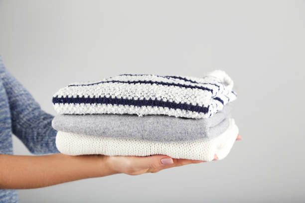 istock Female hands holding folded knitted sweaters on grey background 2205256740