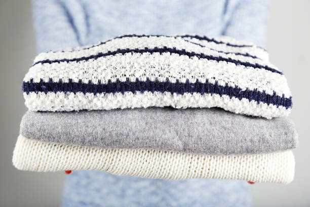 istock Female hands holding folded knitted sweaters on grey background 2205256825