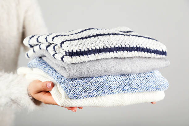 istock Female hands holding folded knitted sweaters on grey background 2205256862